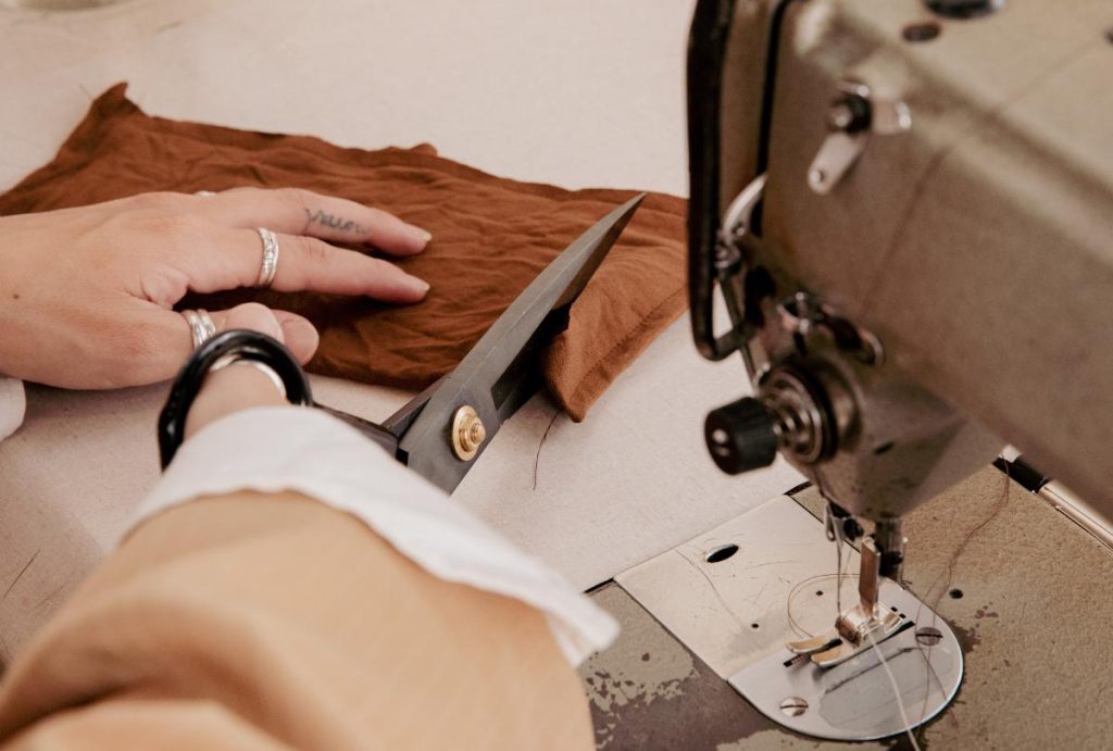 Hands cut fabric beside an industrial machine to imply baby carrier manufacturing