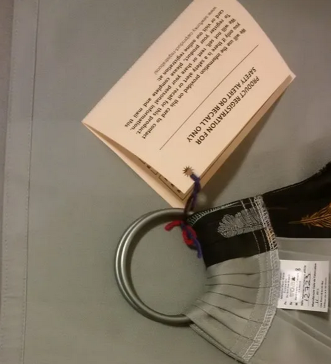 A grey ring sling has a product registration card attached to the rings by a piece of ribbon