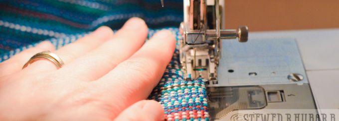 A hand guides a woven wrap design under the presser foot of a sewing machine